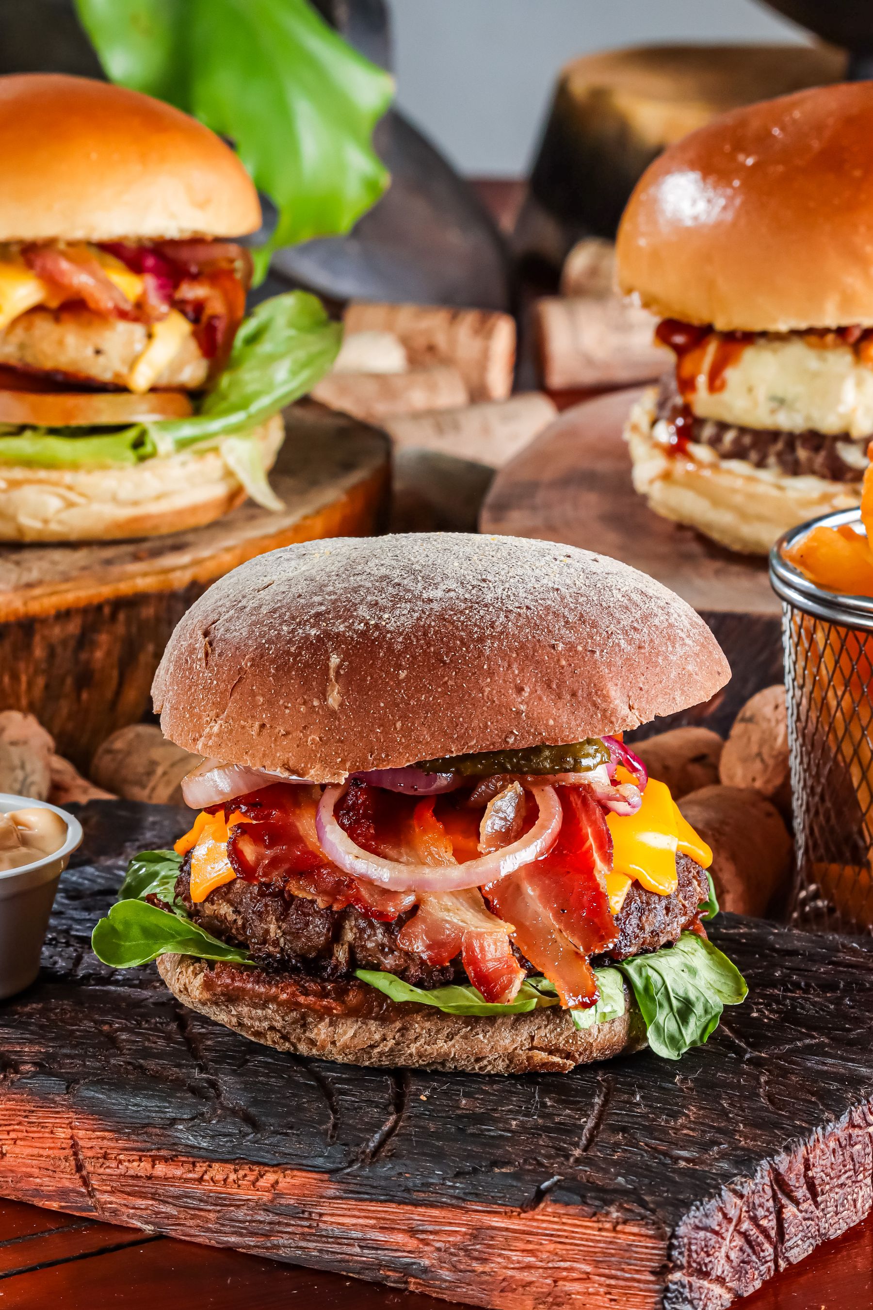 Several gourmet burgers with cheese, bacon, and fresh toppings on wooden boards